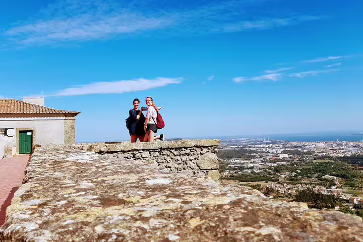 Tourists enjoying scenic views from a historic stone terrace overlooking Lisbon's picturesque southern landscapes and coastline.