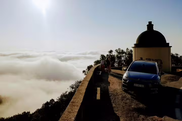 Scenic view from Lisbon's South Sights tour, featuring a car overlooking misty hills and a historic structure under a bright sky.