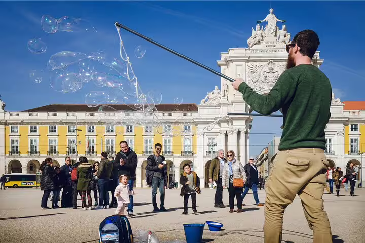 A street performer creates large soap bubbles in Praça do Comércio, Lisbon, captivating tourists on a sunny walking tour.