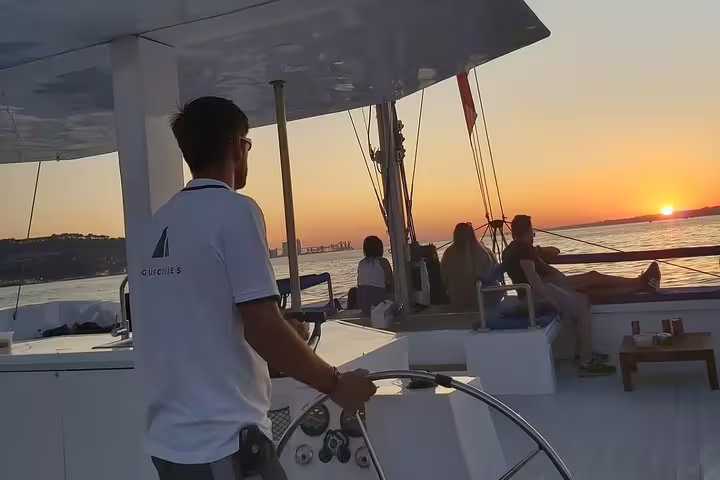 Captain steering a catamaran as passengers relax and watch the sunset on the Tagus River near Lisbon.