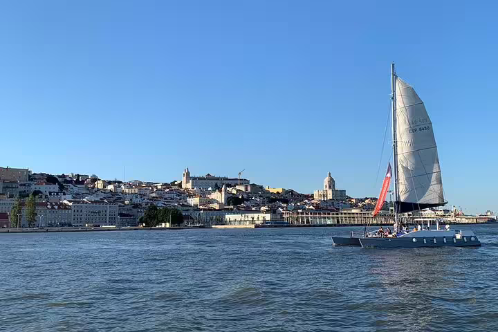 A catamaran glides along the Tagus River with Lisbon's scenic skyline in the background during a sunset cruise.