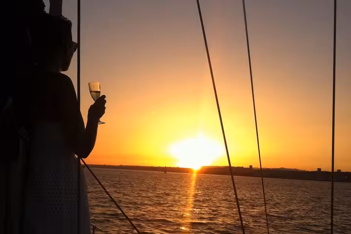 Silhouette holding sparkling wine as the sun sets over the Tagus River on a romantic private Lisbon cruise