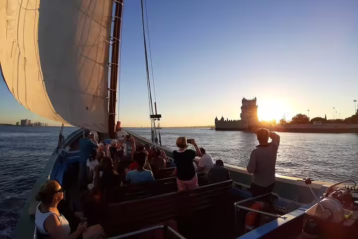 Tourists enjoying a sunset cruise near Lisbon's Belem Tower with white wine on a traditional boat.