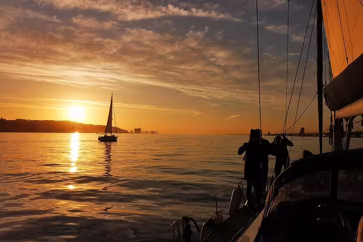 Guests on a luxury yacht watching another sailboat at Lisbon sunset on the Tagus River, sailing tour with 2 drinks
