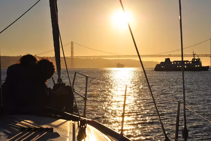 Couple relaxing on sailboat at sunset on Tagus River with 25 de Abril Bridge, Lisbon small group cruise