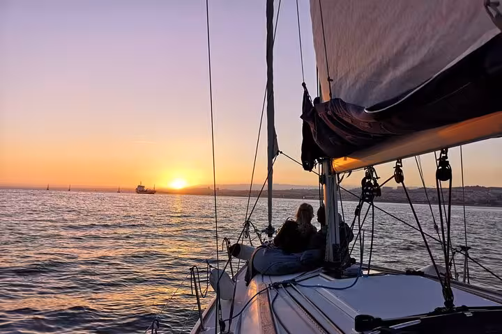Guests relaxing on a sailboat at golden hour during Lisbon sunset sailing cruise on the Tagus River, drink included