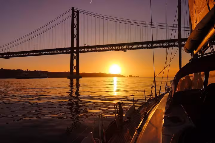 Luxury Lisbon sunset sailing tour passing under 25 de Abril Bridge on the Tagus River, yacht cruise with 2 drinks
