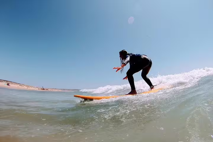Surfer riding a wave on a sunny day in Lisbon, showcasing the thrilling adventure of the Lisbon Surf Experience tour.