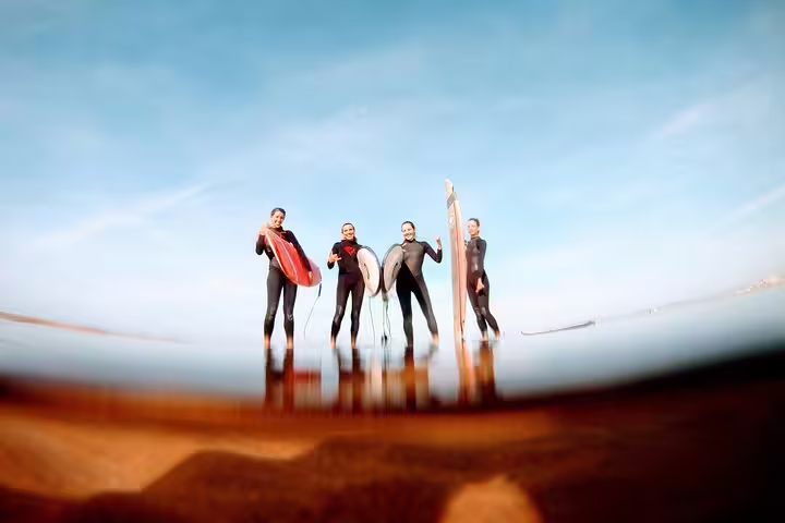 Group of surfers in wetsuits holding boards on a sunny Lisbon beach, enjoying the ultimate surf experience for adventure seekers.