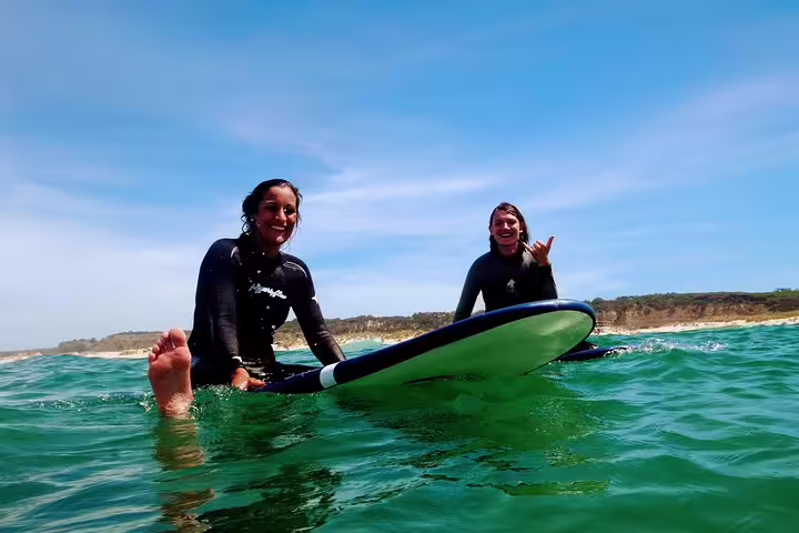Two happy surfers enjoying the clear waters of Lisbon's coast, perfect for the Surf & Wine tour adventure experience.