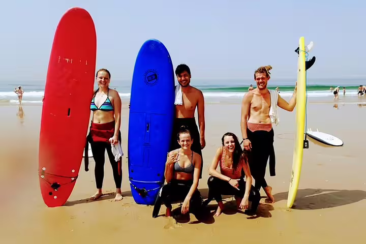 Group of happy surfers with colorful surfboards on a sunny Lisbon beach, perfect for a surf and wine adventure tour.