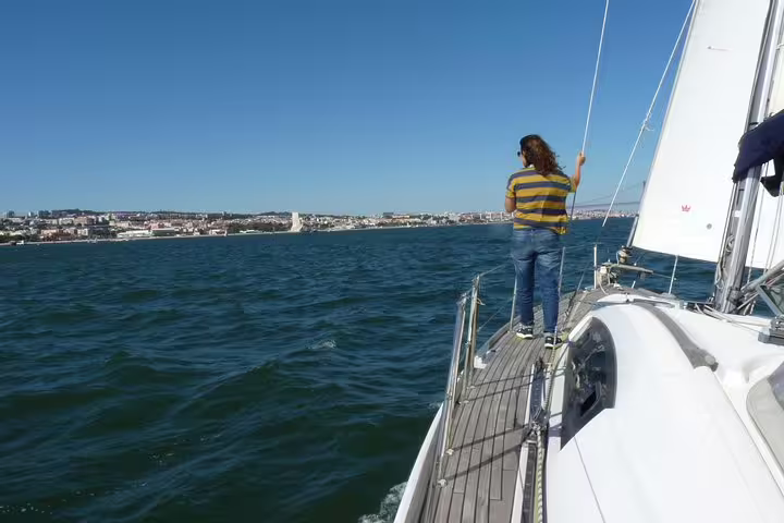 A person stands on the deck of a sailboat gazing at Lisbon's coastline during a Tagus River sailing tour.