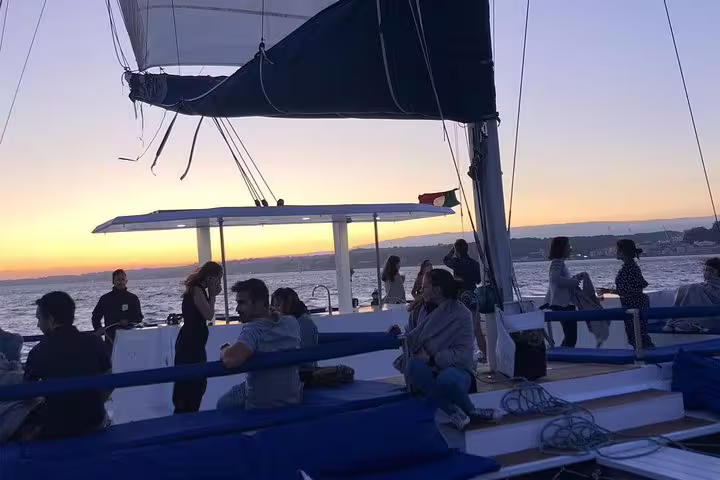 Guests relax on a catamaran at dusk, taking in breathtaking sights during a Lisbon Tagus River sunset cruise.