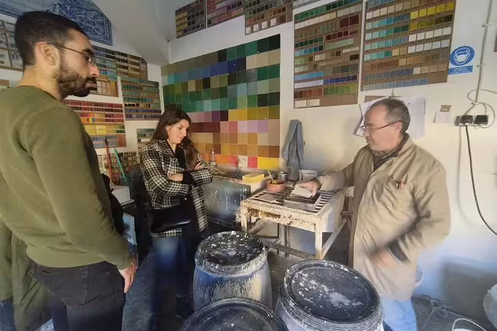 Participants engage in a hands-on tile painting workshop with an expert in a colorful studio during the Sesimbra tour.