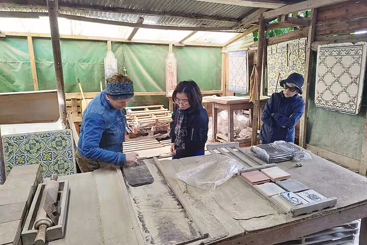 Participants engage in a hands-on tiles painting workshop, part of a private Sesimbra tour with wine tasting, inside a rustic studio.