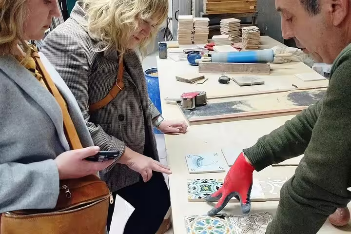 Participants engage in a hands-on tile painting workshop in Sesimbra, learning artistic techniques from a skilled instructor.