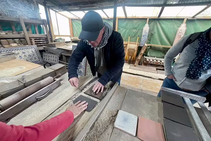 Participants engage in hands-on tile painting during a private workshop, part of a cultural tour with wine tasting in Sesimbra.