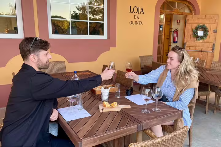 Couple enjoying wine tasting at Loja da Quinta during a private tiles painting workshop and Sesimbra tour on a sunny patio.