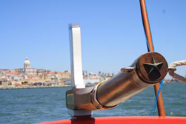 Traditional Lisbon boat with decorative star detail cruising past historic cityscape under a clear blue sky.