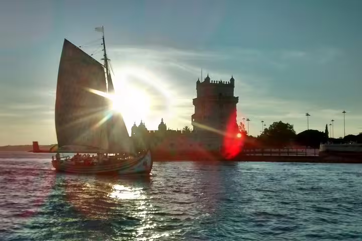 A traditional boat sails by the iconic Belém Tower during a picturesque Lisbon sunset cruise.
