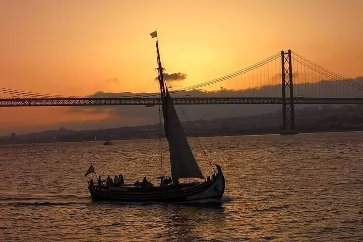 Traditional boat silhouetted against a vibrant sunset near the 25 de Abril Bridge on a Lisbon river cruise.