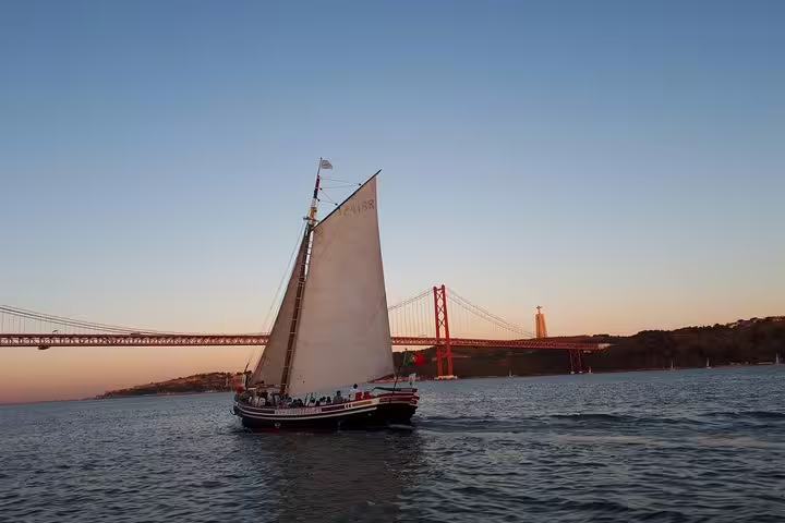 Traditional boat sails past Lisbon's iconic bridge during a sunset cruise with wine, offering breathtaking views.