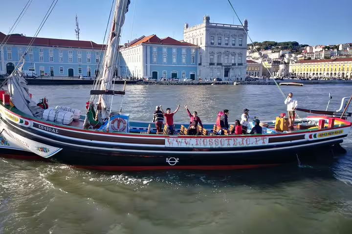 Colorful traditional boat cruising the Tagus River with Lisbon's historic architecture in the background.