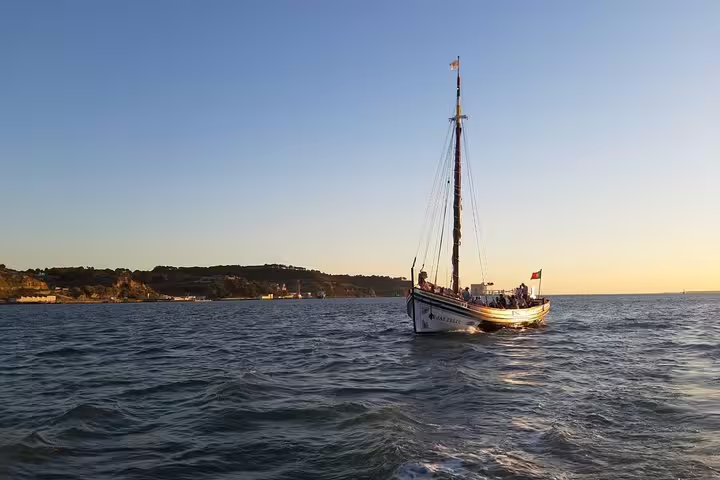 Traditional boat cruising on Lisbon's Tagus River at sunset with scenic coastal views.