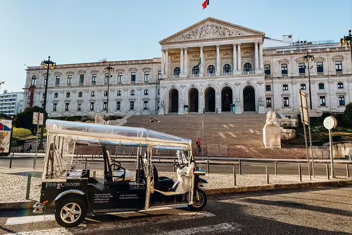 Lisbon tuk-tuk parked in front of the grand São Bento Palace, showcasing architecture on a private city tour.