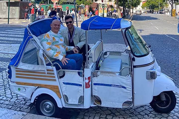 Guests riding a classic tuk tuk on a 1-hour Lisbon Old Town experience, parked on a central city avenue