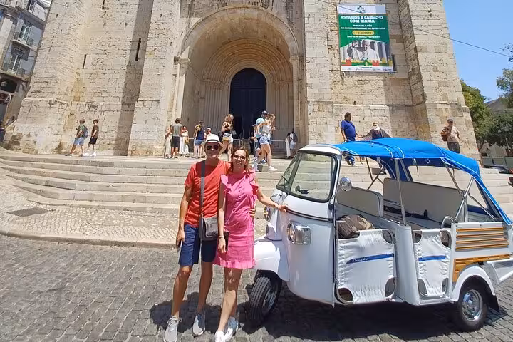 Couple by tuk-tuk at Lisbon Cathedral Sé entrance, highlight of 2-hour tuk-tuk tour paired with sunset sailing cruise