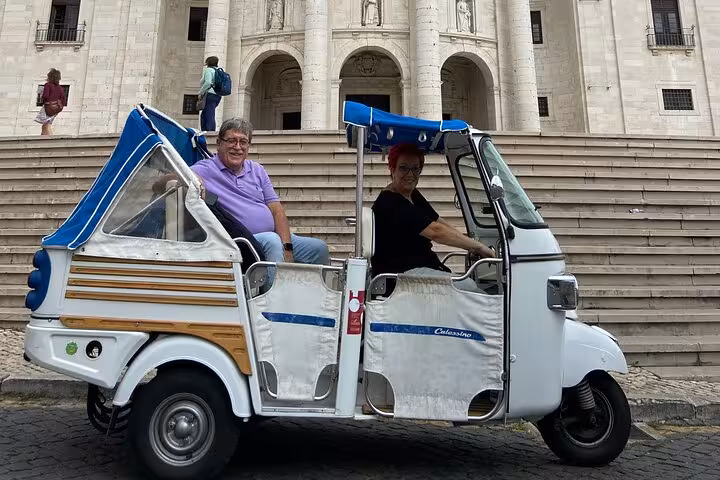 Guests in vintage tuk-tuk at Lisbon Cathedral steps, part of 2-hour tuk-tuk tour and sunset sailing combo