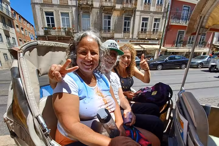 Smiling guests riding a Lisbon tuk-tuk through historic downtown streets during a 2-hour city tour experience