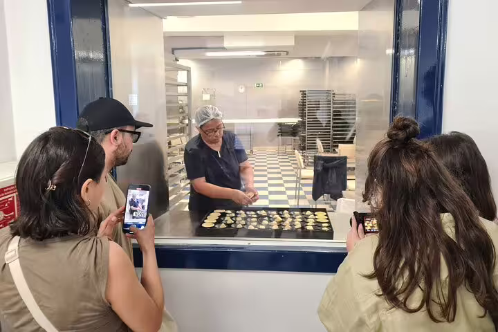Tourists watch a local artisan make traditional Portuguese pastries during a Lisbon TukTuk tour with a local guide.