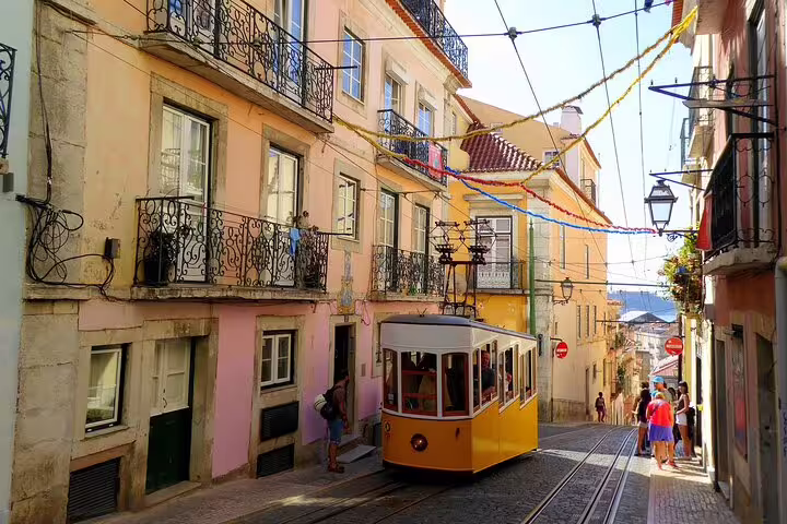 Iconic yellow tram passes through colorful Alfama streets on a Lisbon walking tour.
