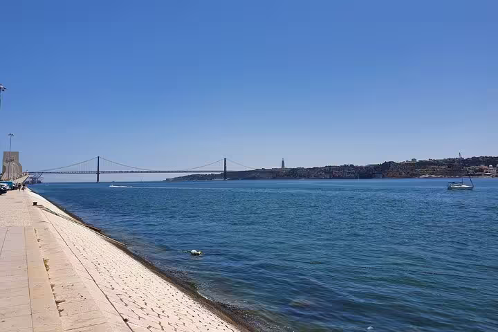 Scenic view of Lisbon's waterfront featuring the iconic 25 de Abril Bridge and river, ideal for the Lisboa full-day tour.