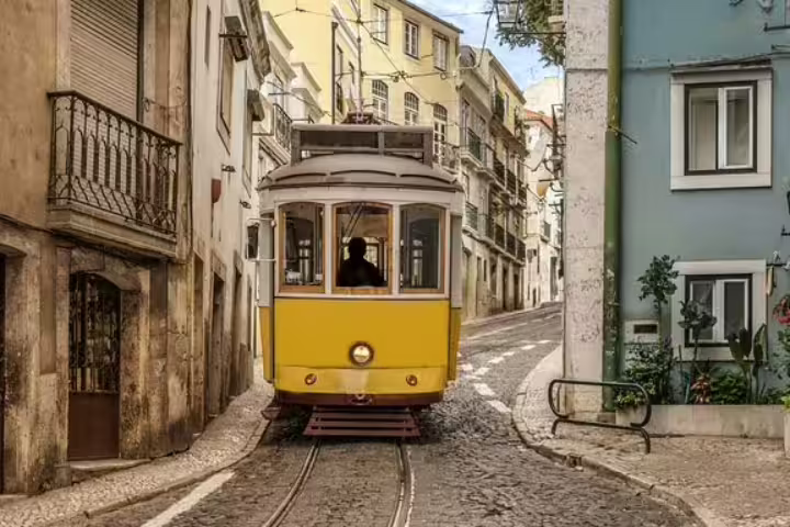 Vintage yellow tram navigates a charming, narrow cobblestone street in Lisbon, showcasing local life away from tourist paths.