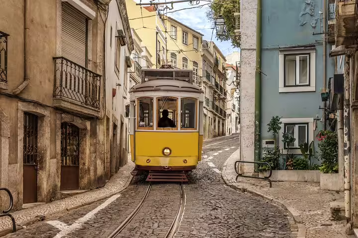 Charming vintage yellow tram navigating narrow cobblestone streets in Lisbon's historic district during a private walking tour.