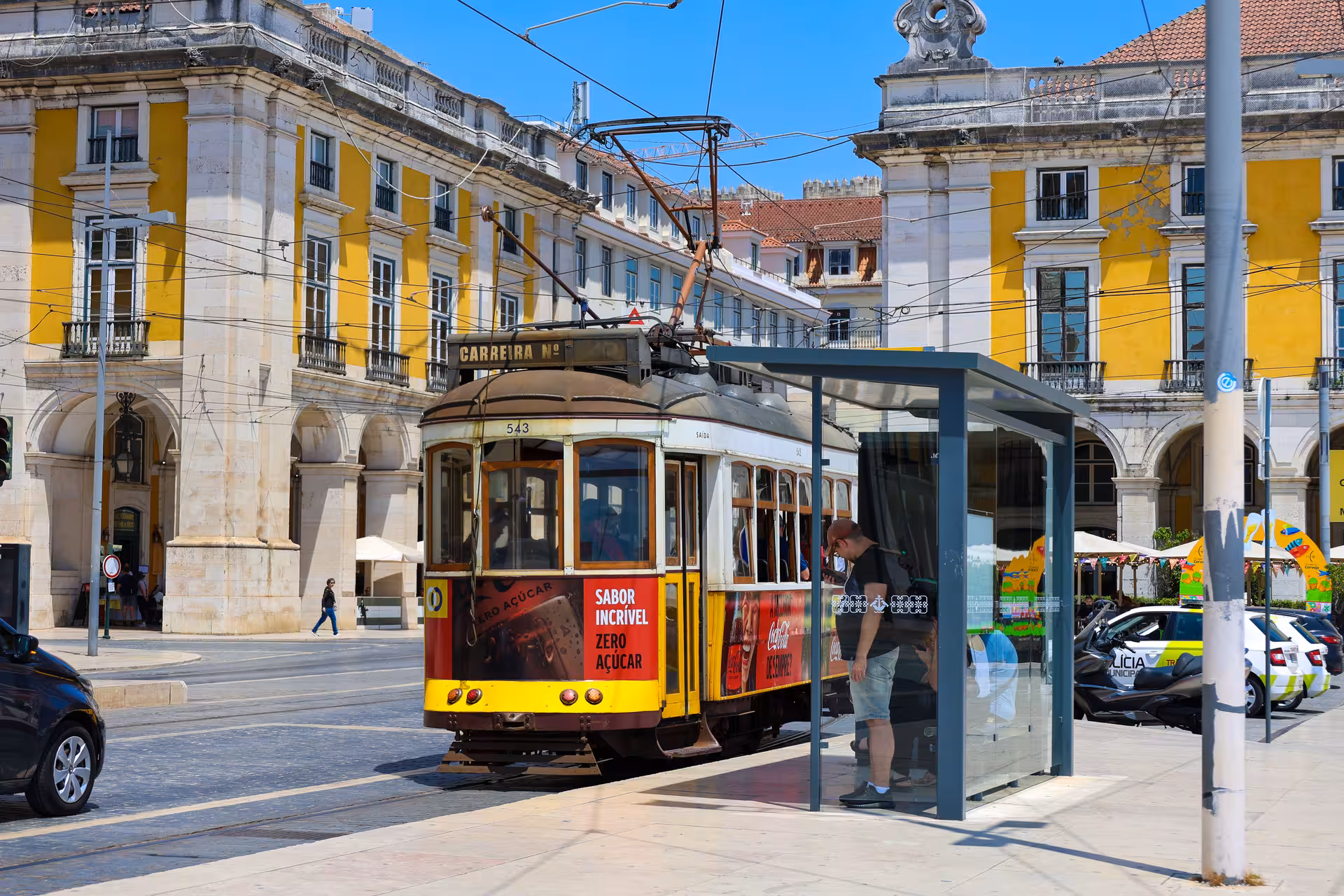 Historic yellow tram passing through Lisbon's iconic Praça do Comércio on a sunny day, perfect for sightseeing tours.