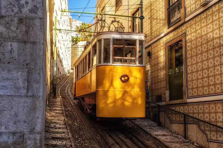 Historic yellow tram ascends a narrow, sunlit street in Lisbon, showcasing the charm of the city on a private walking tour.