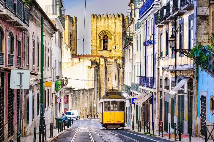 Vintage yellow tram on a vibrant street in Lisbon with a view of the iconic Sé Cathedral in the background.