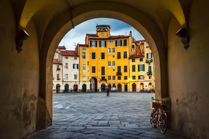 Picturesque archway view of Piazza dell'Anfiteatro in Lucca, highlighting vibrant buildings on a Livorno excursion.