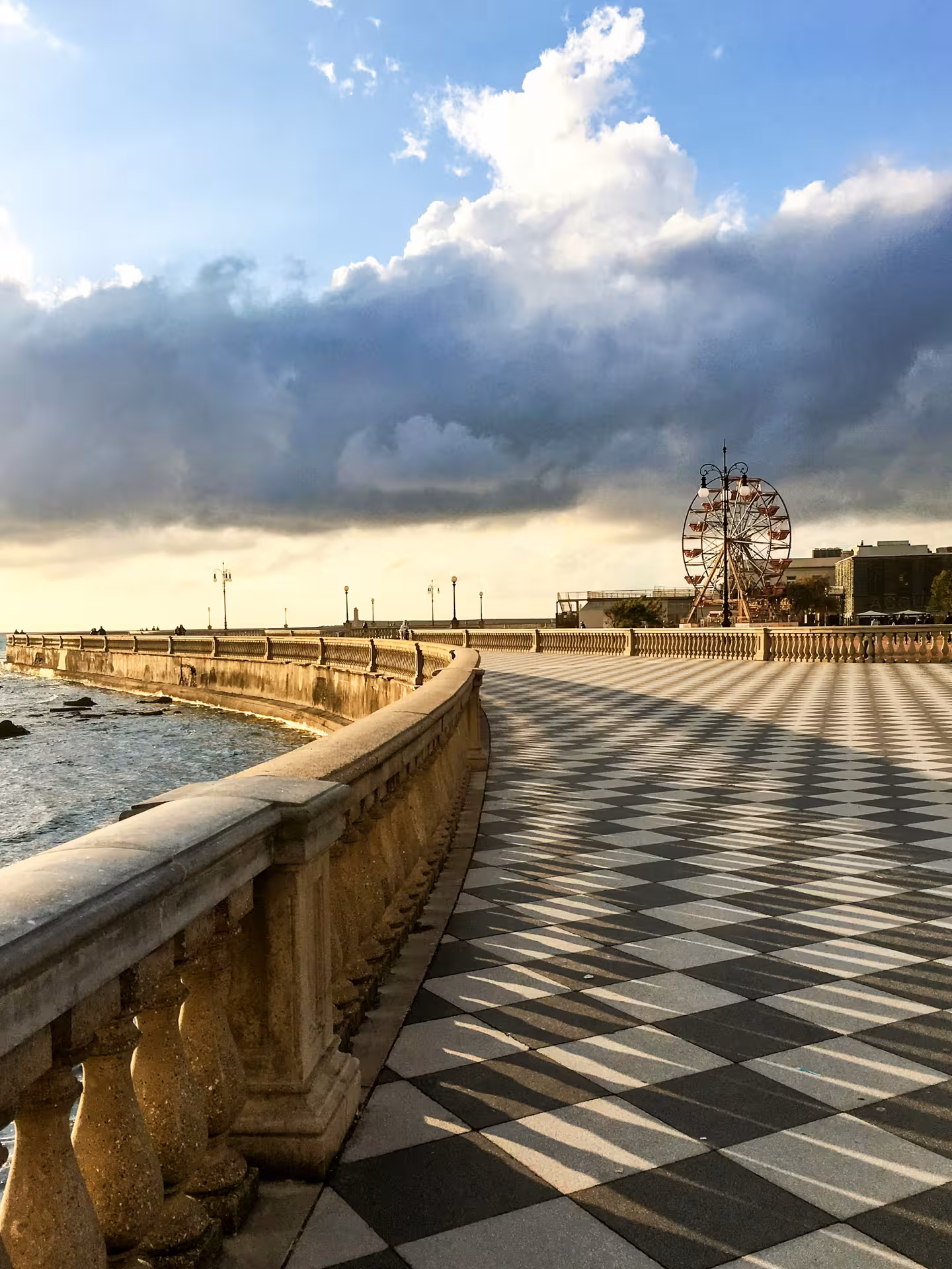 Scenic view of Livorno promenade with a Ferris wheel under a dramatic sky, ideal for Tuscany sunset boat tours.