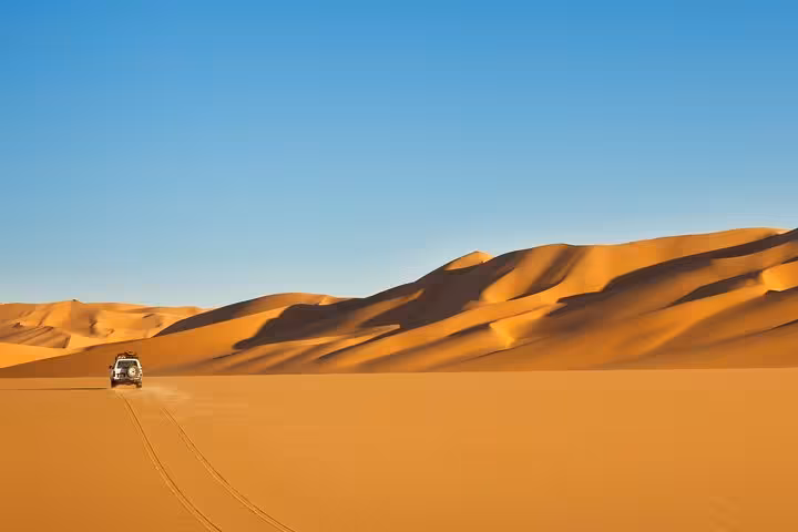 A 4x4 vehicle traverses the endless golden dunes under a clear blue sky on the exhilarating Liwa Desert Safari adventure.
