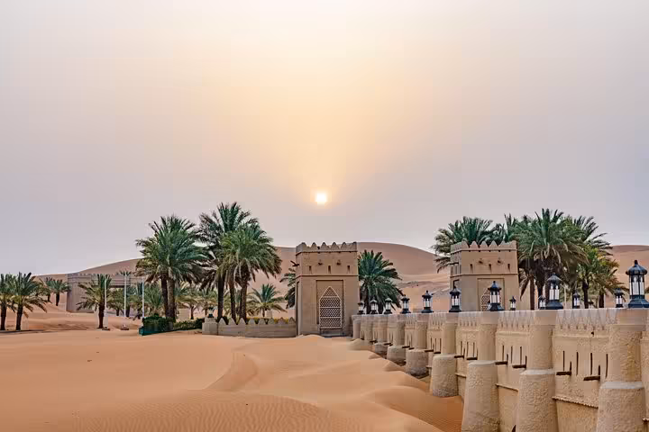 Majestic fort entrance surrounded by palm trees at sunrise in the vast Liwa Desert, perfect for a full day safari.