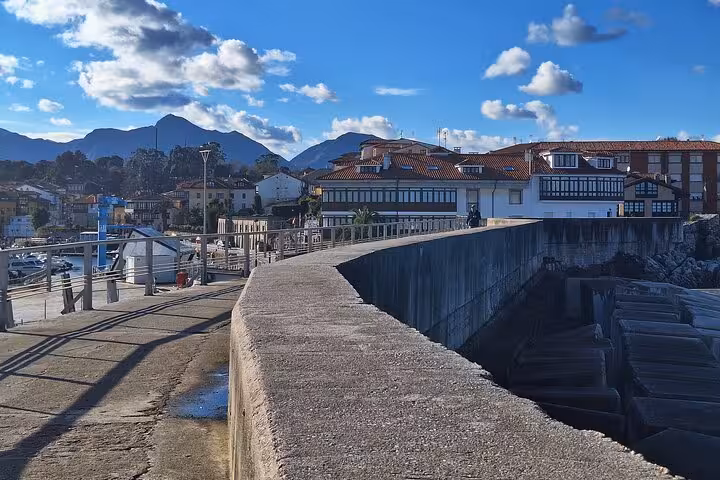Charming coastal view of Llanes with traditional houses and distant mountains under a clear blue sky.
