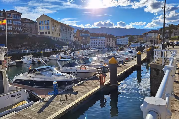 Scenic view of Llanes marina with docked boats and historic buildings under a bright blue sky.
