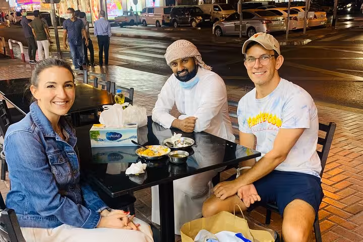Travelers taste local Emirati snacks at outdoor cafe in Old Dubai during 6 tastings walking tour and shopping