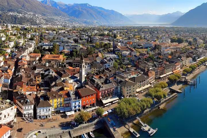 Aerial view of Locarno, showcasing vibrant buildings and serene Lake Maggiore surrounded by mountains.