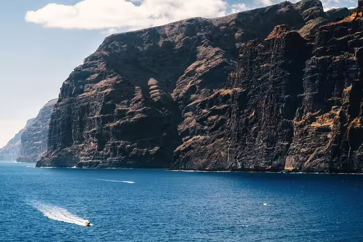 Dramatic cliffs of Los Gigantes towering over the blue ocean in Tenerife, with a small boat nearby.